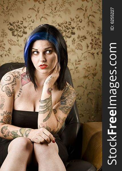 Pretty young woman with many tattoos in a leather chair. Pretty young woman with many tattoos in a leather chair
