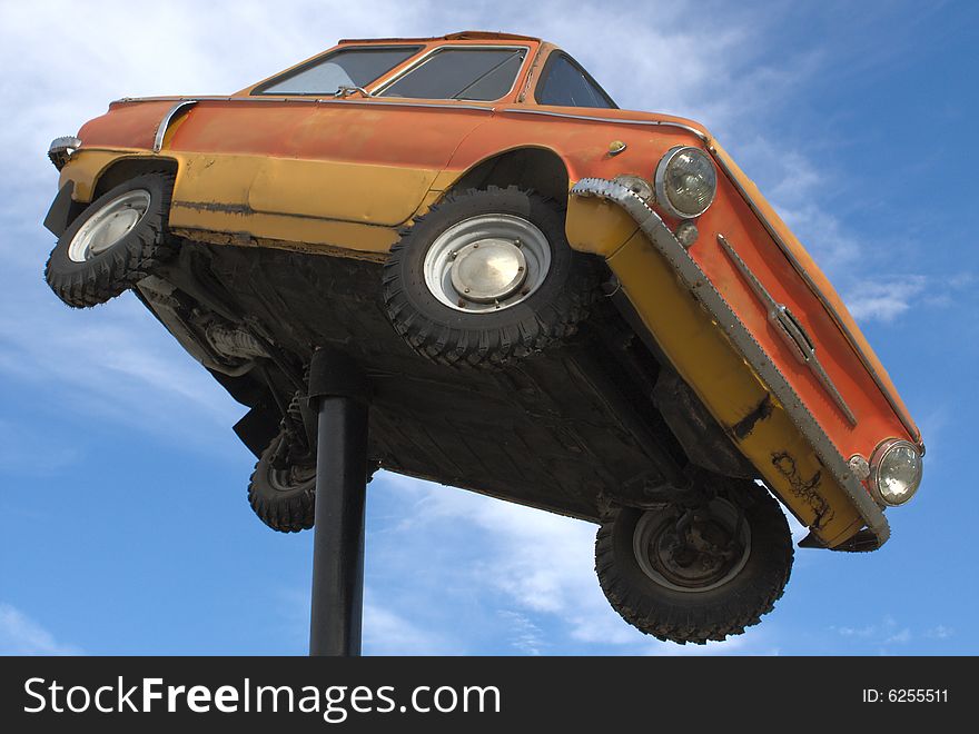 The old automobile on a background of the blue sky with clouds it is yellow - orange color rusty hangs on a pipe