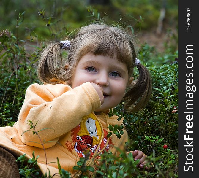 Charmed little girl relaxing in the grass and eating cranberry. Charmed little girl relaxing in the grass and eating cranberry.