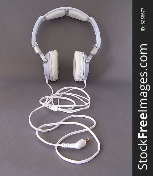 White padded headphones with white cable snaking into foreground. White padded headphones with white cable snaking into foreground.