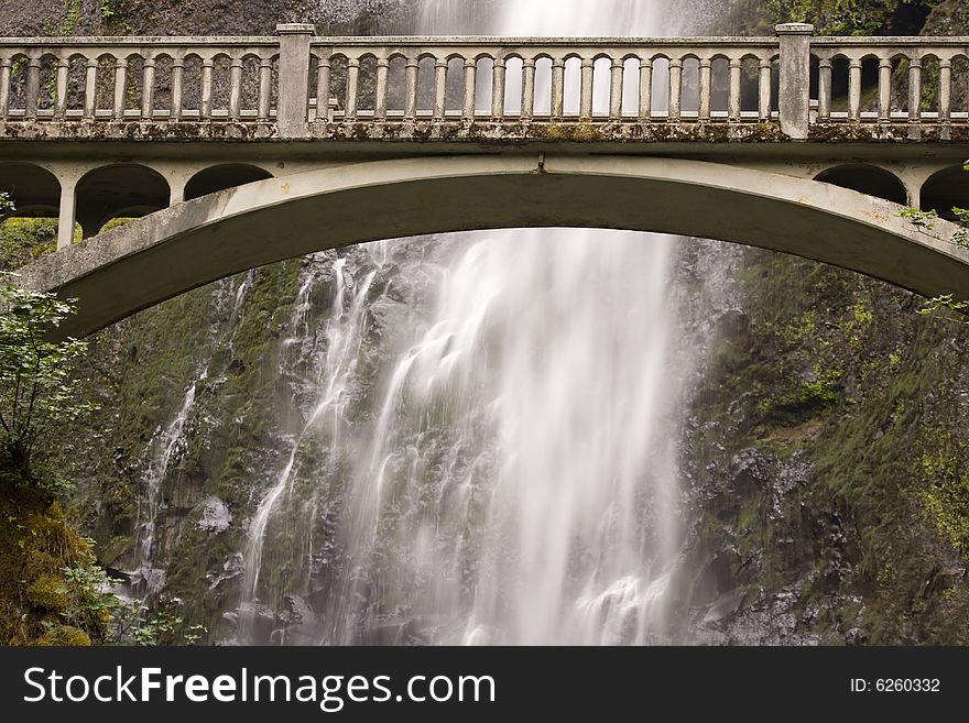 Arched bridge with cascading waterall against mountain rocks. Arched bridge with cascading waterall against mountain rocks