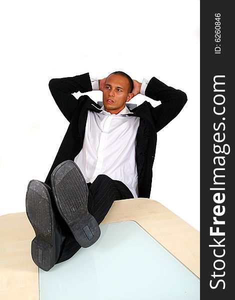 A young satisfied businessman sitting by desk at office feet on table thinking. Isolated over white. A young satisfied businessman sitting by desk at office feet on table thinking. Isolated over white.