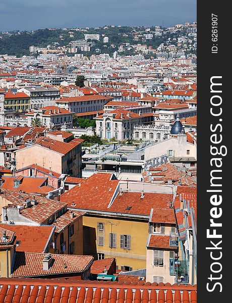 Red tile roofs in old district of Nice, buildings and edifices with white and yellow walls, dark green hills and blue sky behind, view from above. Red tile roofs in old district of Nice, buildings and edifices with white and yellow walls, dark green hills and blue sky behind, view from above