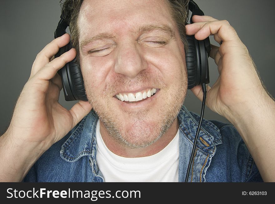 Man with Eyes Shut Wearing Headphones Enjoying His Music on a Grey Background. Man with Eyes Shut Wearing Headphones Enjoying His Music on a Grey Background.