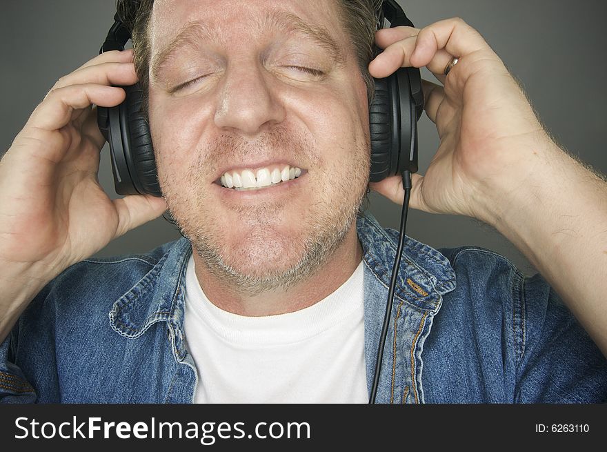 Man with Eyes Shut Wearing Headphones Enjoying His Music on a Grey Background. Man with Eyes Shut Wearing Headphones Enjoying His Music on a Grey Background.