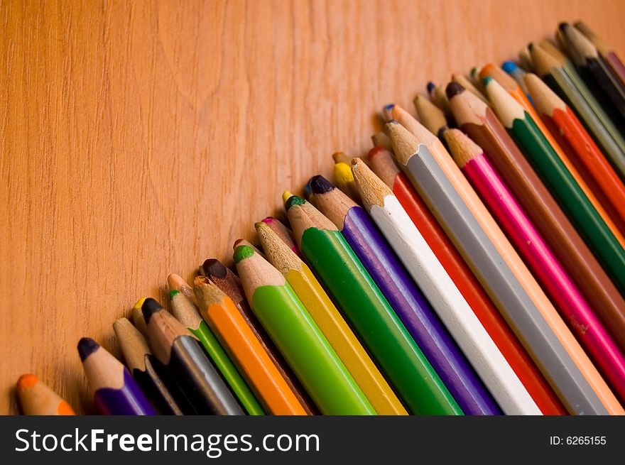 Many color pencils lay on a wooden surface. Many color pencils lay on a wooden surface