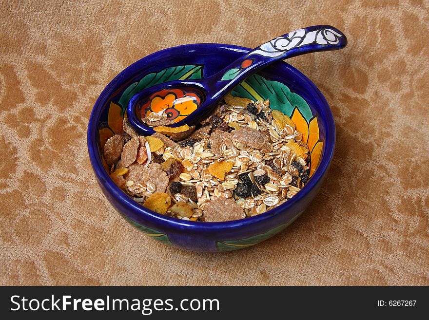 Flower pattern colored ceramic bowl and spoon with cereal on a brown velvet background. Flower pattern colored ceramic bowl and spoon with cereal on a brown velvet background.