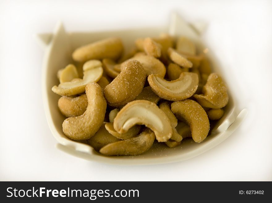 A pile of cashew nuts in a bowl isolated on a white background. The focus is selective