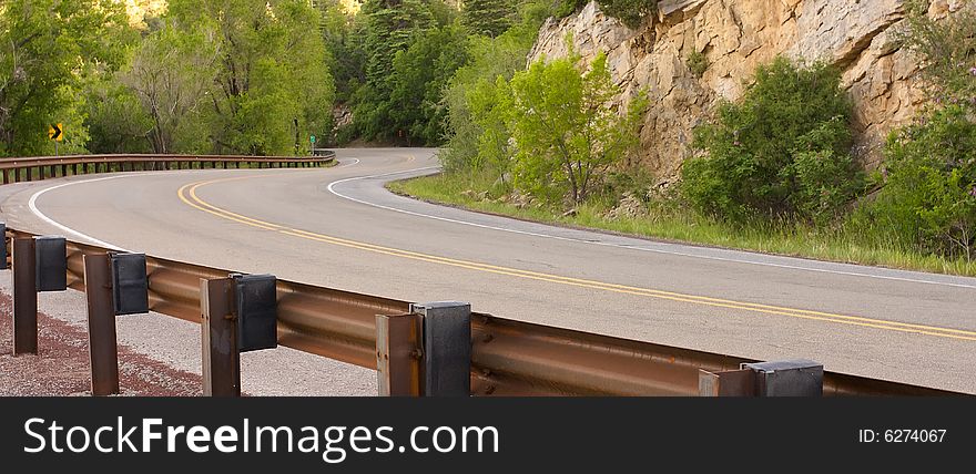 An image of a curving road surrounded by mountains and foliage. An image of a curving road surrounded by mountains and foliage