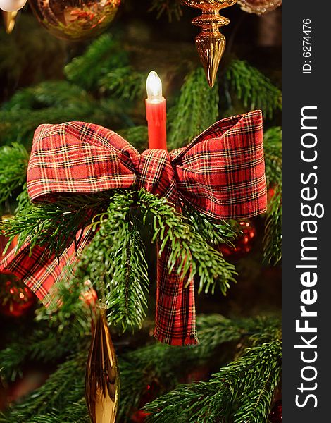 Part of a decorated christmas tree with candle and checkered ribbon