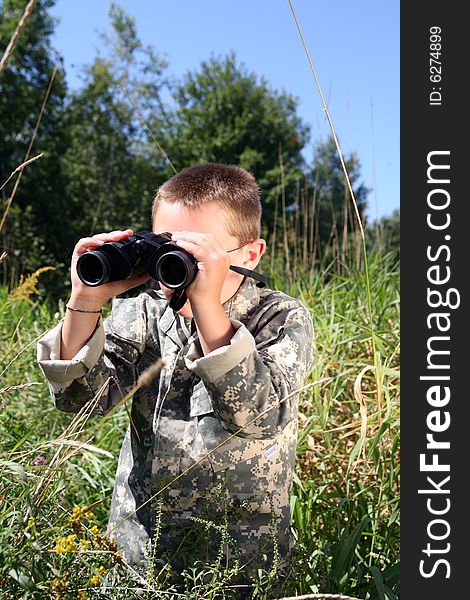 Young boy in camoflage, looking through binoculars in a field