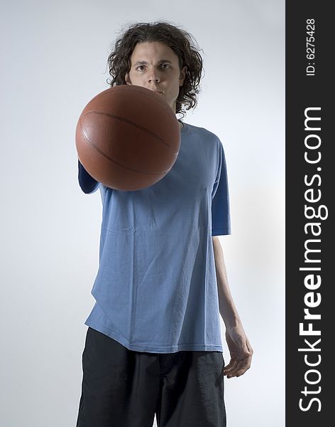 An athlete holding a basket ball with a straight arm.  He is looking at the camera.  He has a serious expression on his face. Vertically framed shot. An athlete holding a basket ball with a straight arm.  He is looking at the camera.  He has a serious expression on his face. Vertically framed shot.