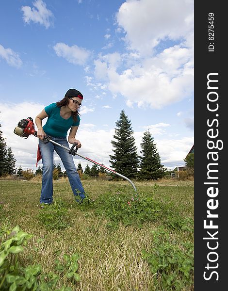 Angry woman standing in a field using a weedwacker. Vertically framed photo. Angry woman standing in a field using a weedwacker. Vertically framed photo.