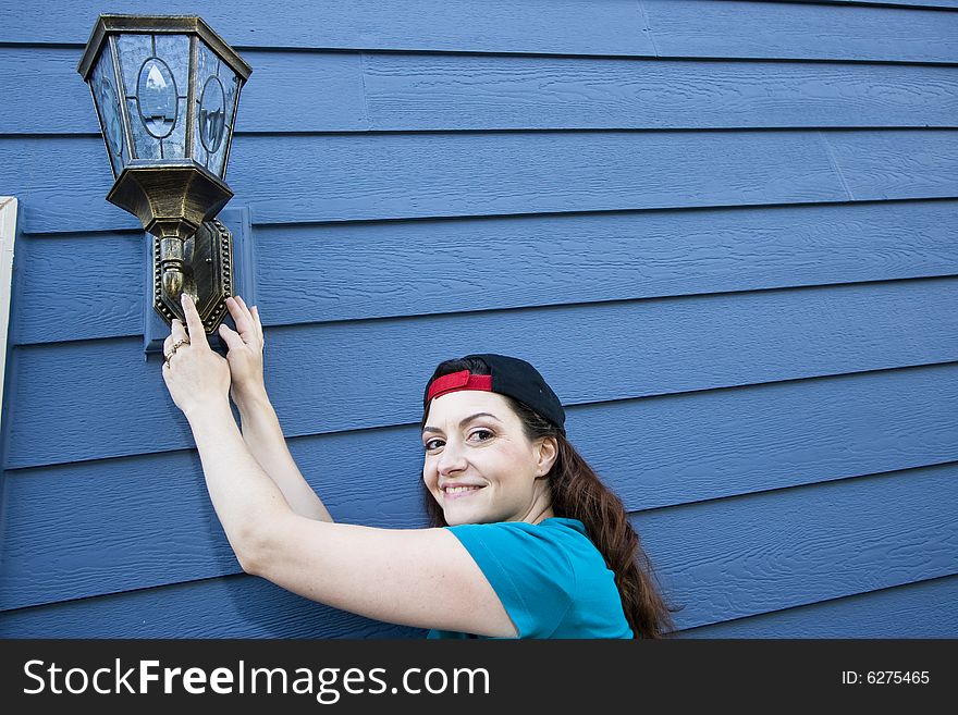 Smiling woman hanging a light fixture on a house. Horizontally framed photo. Smiling woman hanging a light fixture on a house. Horizontally framed photo.
