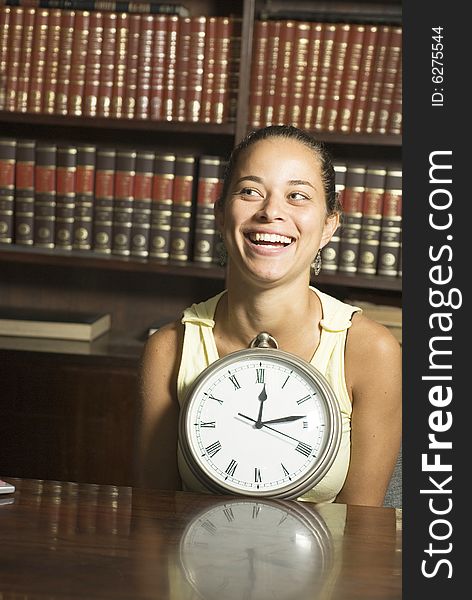 Smiling woman at desk in office with clock. Vertically framed photo. Smiling woman at desk in office with clock. Vertically framed photo.