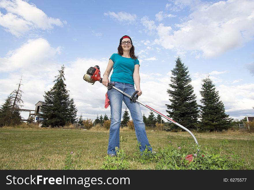 Smiling woman standing in a field using a weedwacker. Horizontally framed photo. Smiling woman standing in a field using a weedwacker. Horizontally framed photo.