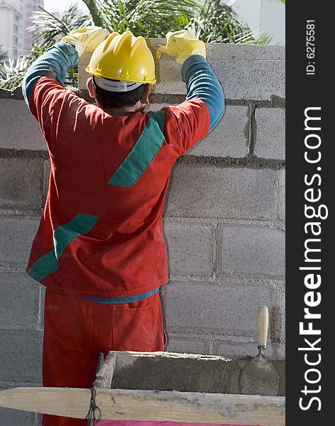 The worker is standing in front of the wall.  He is assembling more cinder blocks to the wall.  Vertically framed shot. The worker is standing in front of the wall.  He is assembling more cinder blocks to the wall.  Vertically framed shot.