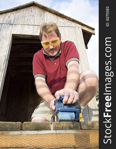 Man wearing safety glasses uses a power sander on wood. Vertically framed photo. Man wearing safety glasses uses a power sander on wood. Vertically framed photo.