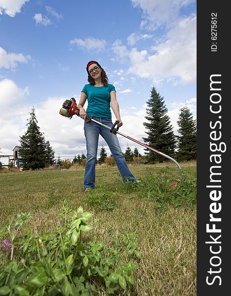 Smiling woman standing in a field using a weedwacker. Vertically framed photo. Smiling woman standing in a field using a weedwacker. Vertically framed photo.