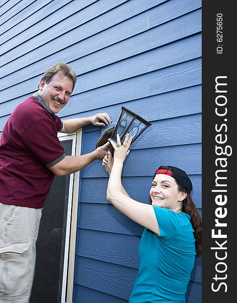 Happy couple hanging a light fixture on a house. Vertically framed photo. Happy couple hanging a light fixture on a house. Vertically framed photo.