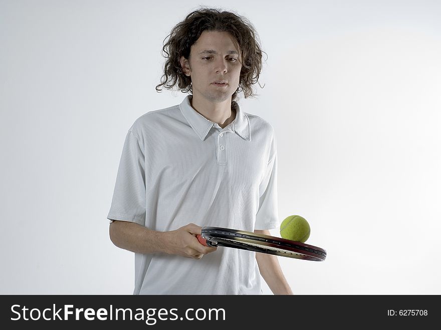 A young man balancing a tennis ball on a racket.  He is focusing on the ball and has a serious expression on his face. Horizontally framed shot. A young man balancing a tennis ball on a racket.  He is focusing on the ball and has a serious expression on his face. Horizontally framed shot.