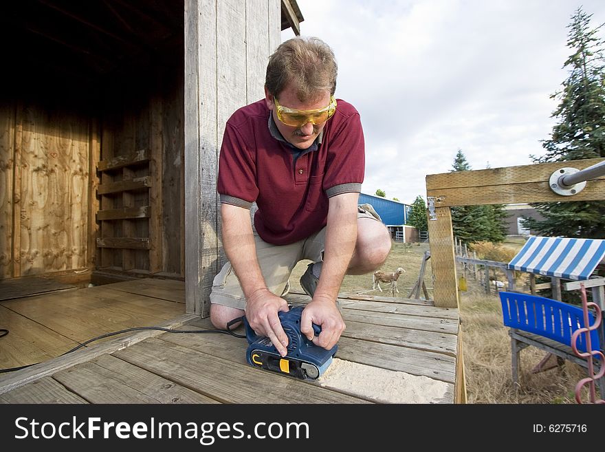 Smiling man with safety glasses using a power sander on some wood. Horizontally framed photo. Smiling man with safety glasses using a power sander on some wood. Horizontally framed photo.