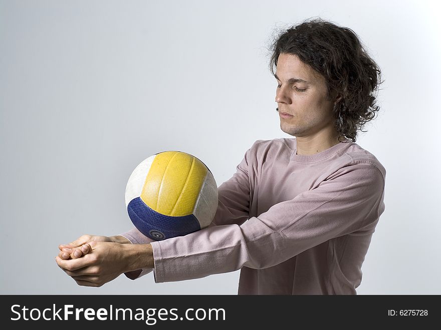 An athlete balancing a volleyball on his forearms. His hands are clasped and his eyes are closed in concentration.  He has a serious expression on his face. Horizontally framed shot. An athlete balancing a volleyball on his forearms. His hands are clasped and his eyes are closed in concentration.  He has a serious expression on his face. Horizontally framed shot.