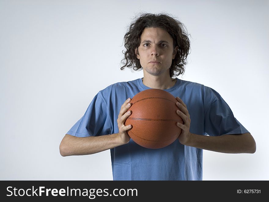 A young man holding a basketball.  He is looking at the camera.  He has a serious expression on his face. Horizontally framed shot. A young man holding a basketball.  He is looking at the camera.  He has a serious expression on his face. Horizontally framed shot.