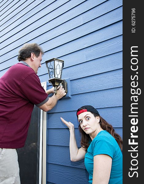 Happy couple hanging a light fixture on a house. The woman looks frustrated. Vertically framed photo. Happy couple hanging a light fixture on a house. The woman looks frustrated. Vertically framed photo.