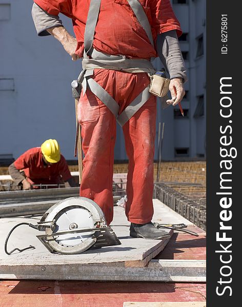 The worker is standing behind a circular saw. There is another worker in the background. Vertically framed shot. The worker is standing behind a circular saw. There is another worker in the background. Vertically framed shot.