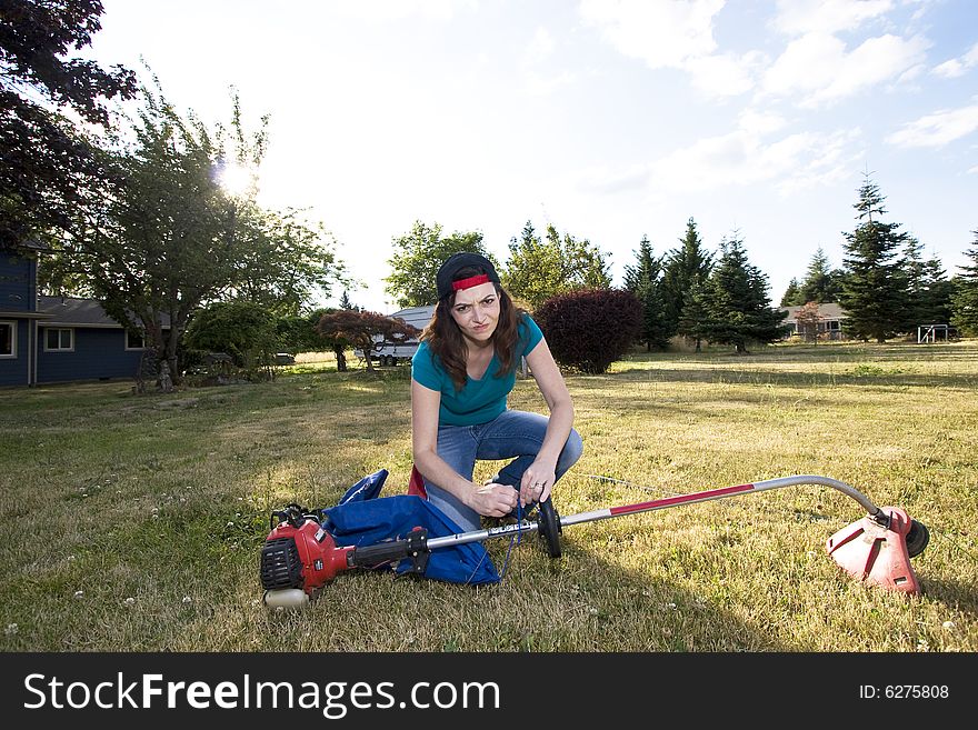 Sneering woman crouches in a field with a weedwacker. Horizontally framed photo. Sneering woman crouches in a field with a weedwacker. Horizontally framed photo.