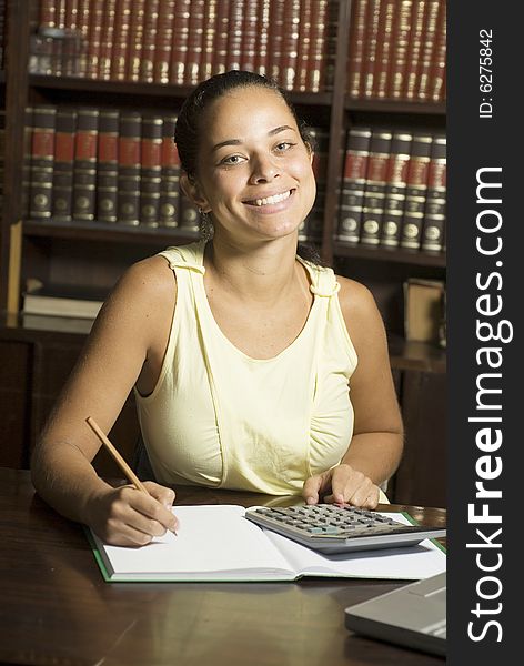 Female student smiling as she sits at a desk writing and using a calculator. Vertically framed photo. Female student smiling as she sits at a desk writing and using a calculator. Vertically framed photo.