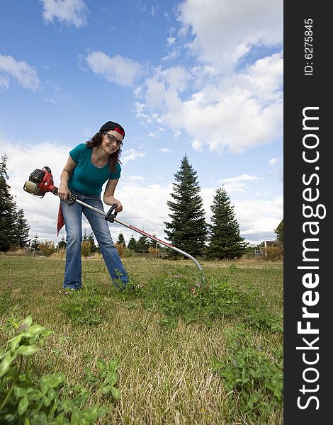 Smiling woman standing in a field using a weedwacker. Vertically framed photo. Smiling woman standing in a field using a weedwacker. Vertically framed photo.