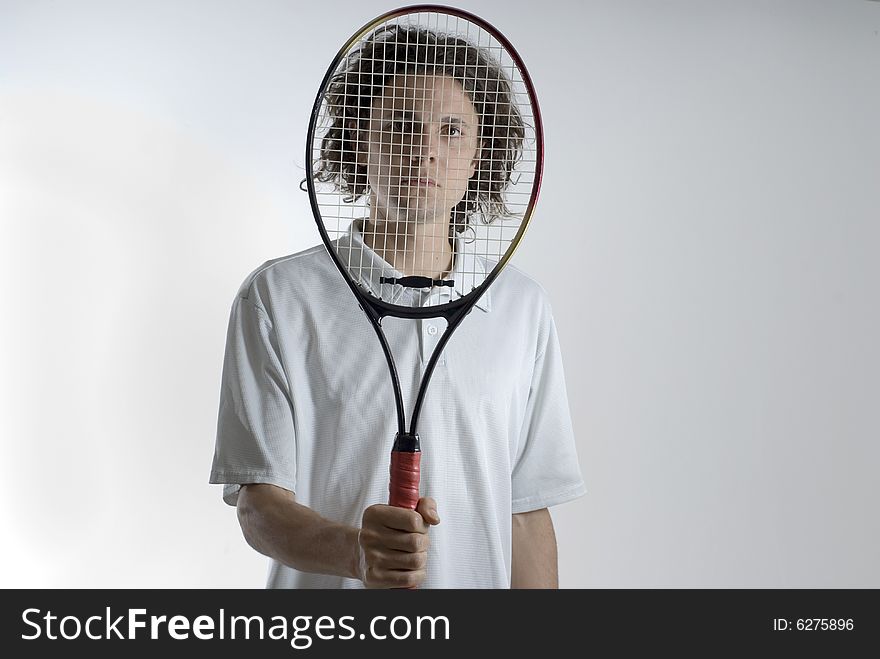 An athlete holding a tennis racket over his face.  He is looking through the racket at the camera.  He has a serious expression on his face. Horizontally framed shot. An athlete holding a tennis racket over his face.  He is looking through the racket at the camera.  He has a serious expression on his face. Horizontally framed shot.