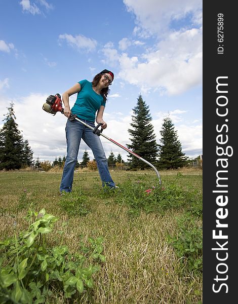 Angry woman standing in a field using a weedwacker. Vertically framed photo. Angry woman standing in a field using a weedwacker. Vertically framed photo.