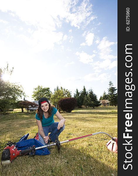 Sneering woman crouches in a field with a weedwacker. Vertically framed photo. Sneering woman crouches in a field with a weedwacker. Vertically framed photo.