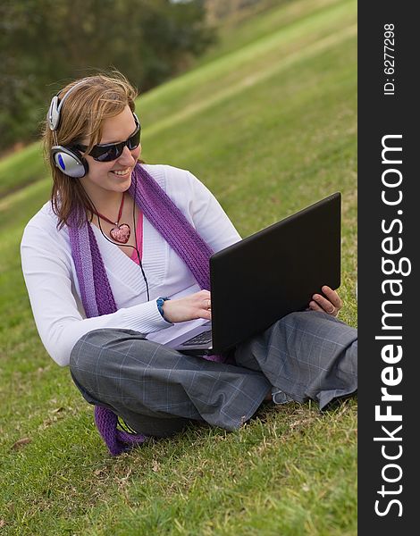 Woman with notebook and earphones sitting on the gras. Woman with notebook and earphones sitting on the gras