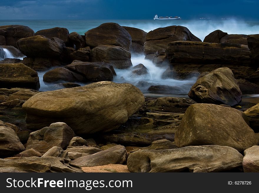 Large rocks on beach with incoming waves and ships in deep ocean water. Large rocks on beach with incoming waves and ships in deep ocean water