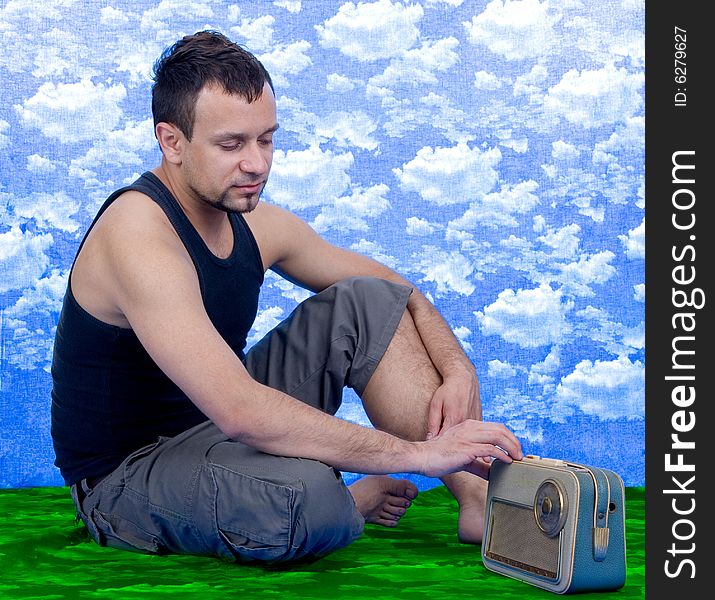 Young man sitting on green grass and listening radio