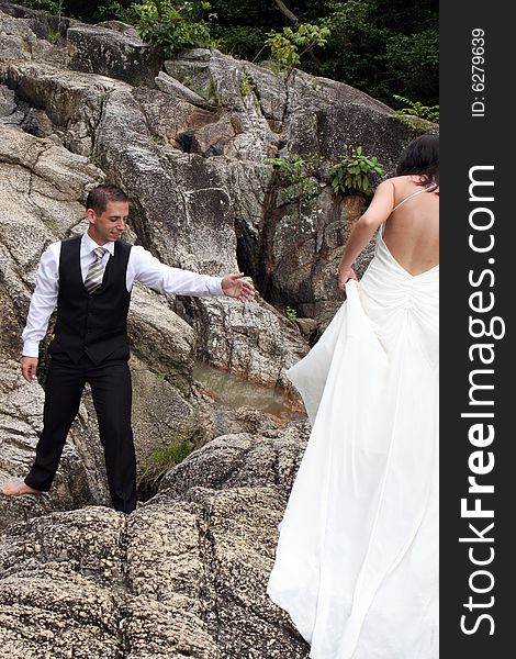 Groom reaches out to help his bride over steep rocks. Groom reaches out to help his bride over steep rocks.
