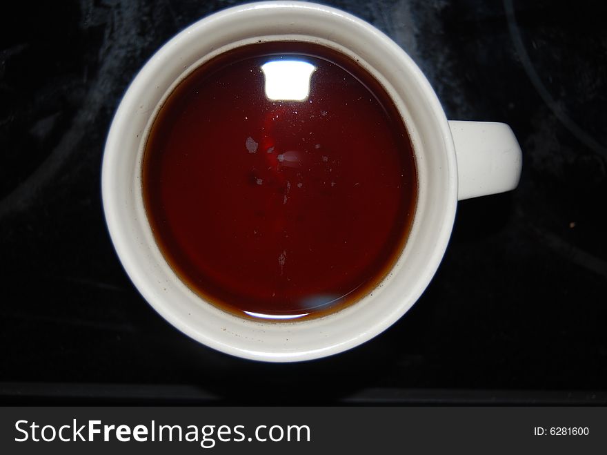 A cup of black Tea with Honey in a white cup on a black table. A cup of black Tea with Honey in a white cup on a black table