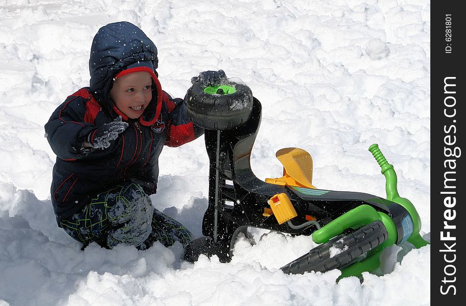 Young boy hiding from snowballs behind a three wheeled toy in the snow. Young boy hiding from snowballs behind a three wheeled toy in the snow