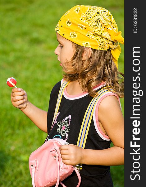 Closeup portrait of little girl with lollipop and bag on green grass. Closeup portrait of little girl with lollipop and bag on green grass