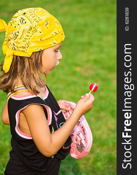 Closeup portrait of little girl with lollipop and bag on green grass. Closeup portrait of little girl with lollipop and bag on green grass