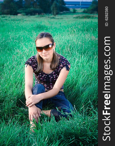 Young girl in sunglasses is sitting in grass. Young girl in sunglasses is sitting in grass