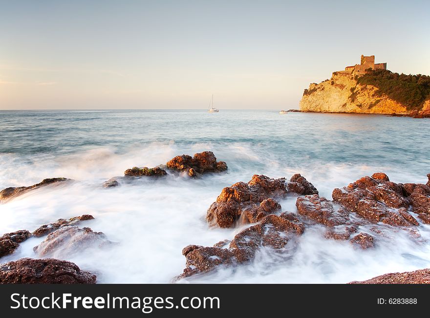 Seaside landscape: sea over rocks, in background the castle of Castiglione, Tuscany, Italy.