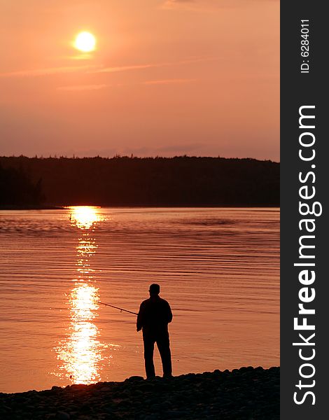 The silhouette of a man fishing at sunset.