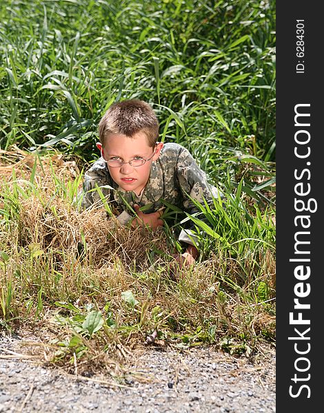 Young boy in cammoflage crawling out of the grass. Young boy in cammoflage crawling out of the grass