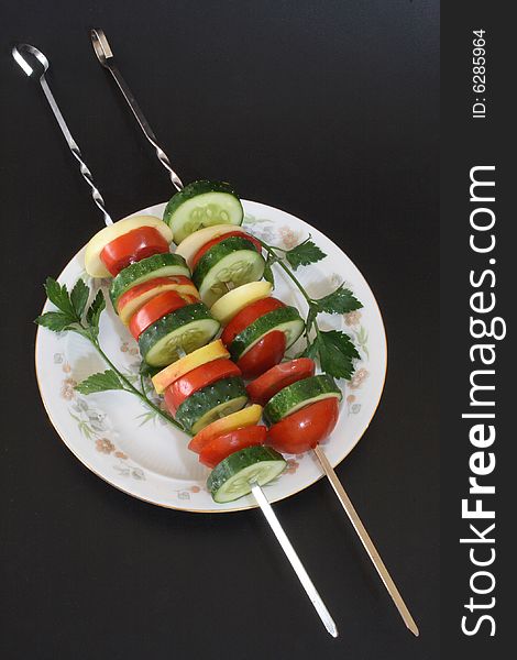 Salad from fresh vegetables on a plate on a black background