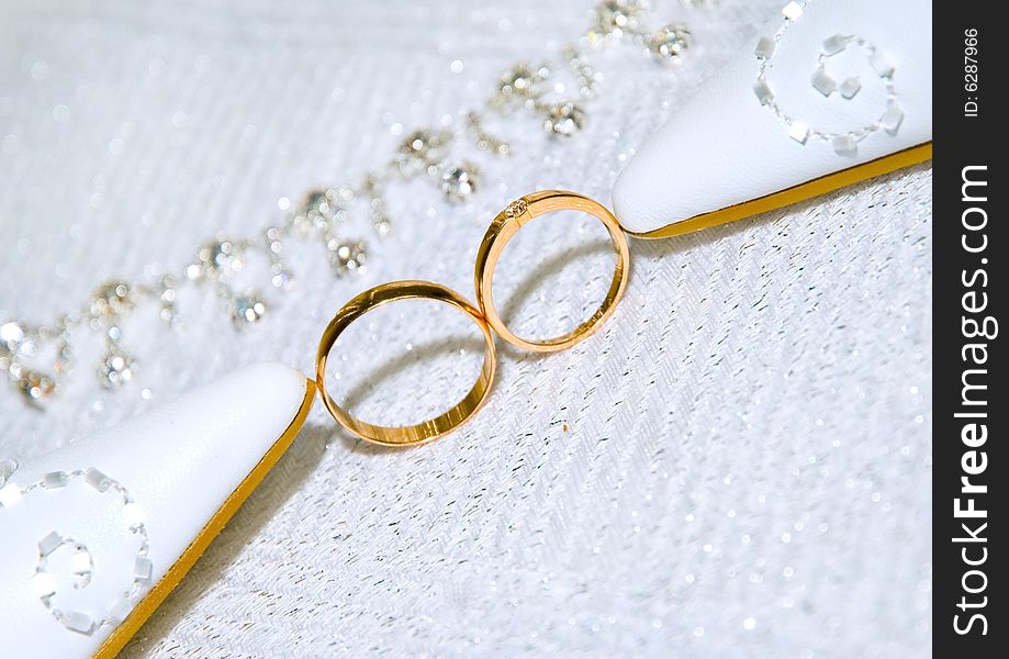 Two gold wedding rings standing together between bride's shoes